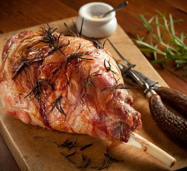 Upečené jahňacie stehno posypané rozmarínom a cesnakom Kombinácia jedál-recepty-jahňacie-mäso-kúsky-špicaté-rozmarínu-vetvičky-soľ-nôž-misa-lyžica-doska na krájanie