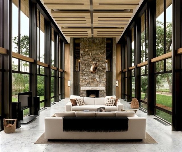 Moderný vidiecky štýl - obývačka so stenou z prírodného kameňa a sedacou súpravou úzka obývačka zariadená sedacími súpravami dom v presklenej lesnej fasáde
