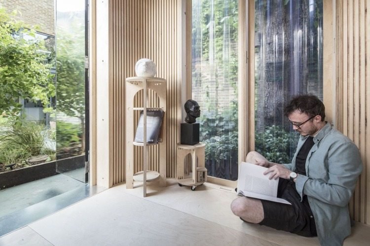 priestor na sedenie a prácu v samostatne postavenej domácej kancelárii s drevenými policami a preglejkovou podlahou