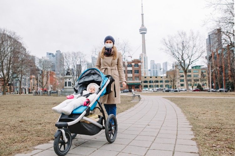 matka s ochrannou maskou a kočíkom kráča v parku počas pandémie COVID-19