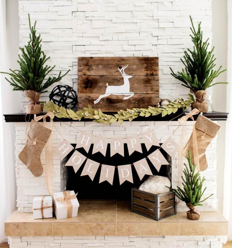 štýlová, domáca dekorácia pri krbe v bielej a béžovej farbe vianočné dekorácie-krb-biely-kamenný obklad-girlanda-jeleň-doska-béžová-štýlová