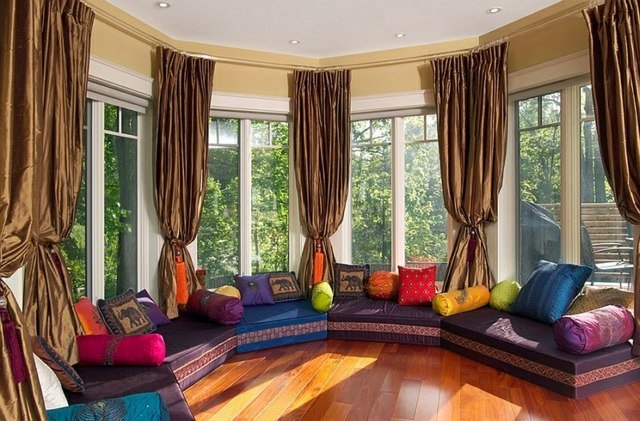 Závesy na okne, drevená podlaha, posedenie v orientálnom štýle Okrúhle sedenie s čalúnením a vankúšmi v arabskom štýle