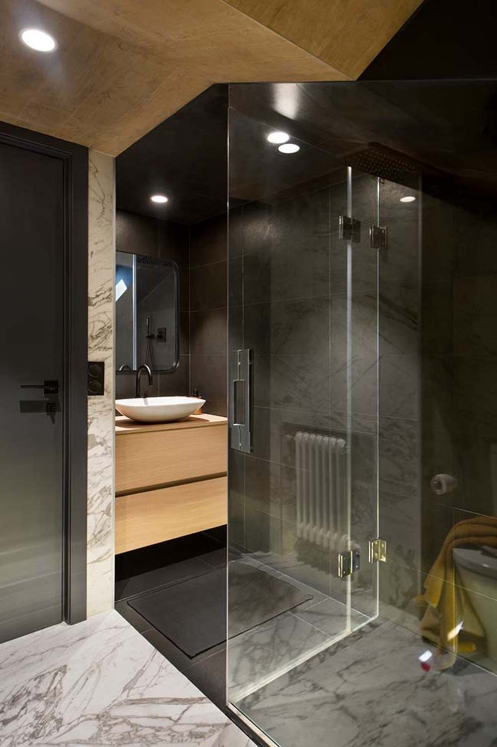 malá kúpeľňa s tmavými dlaždicami a dreveným umývadlom oproti sprchovaciemu kútu