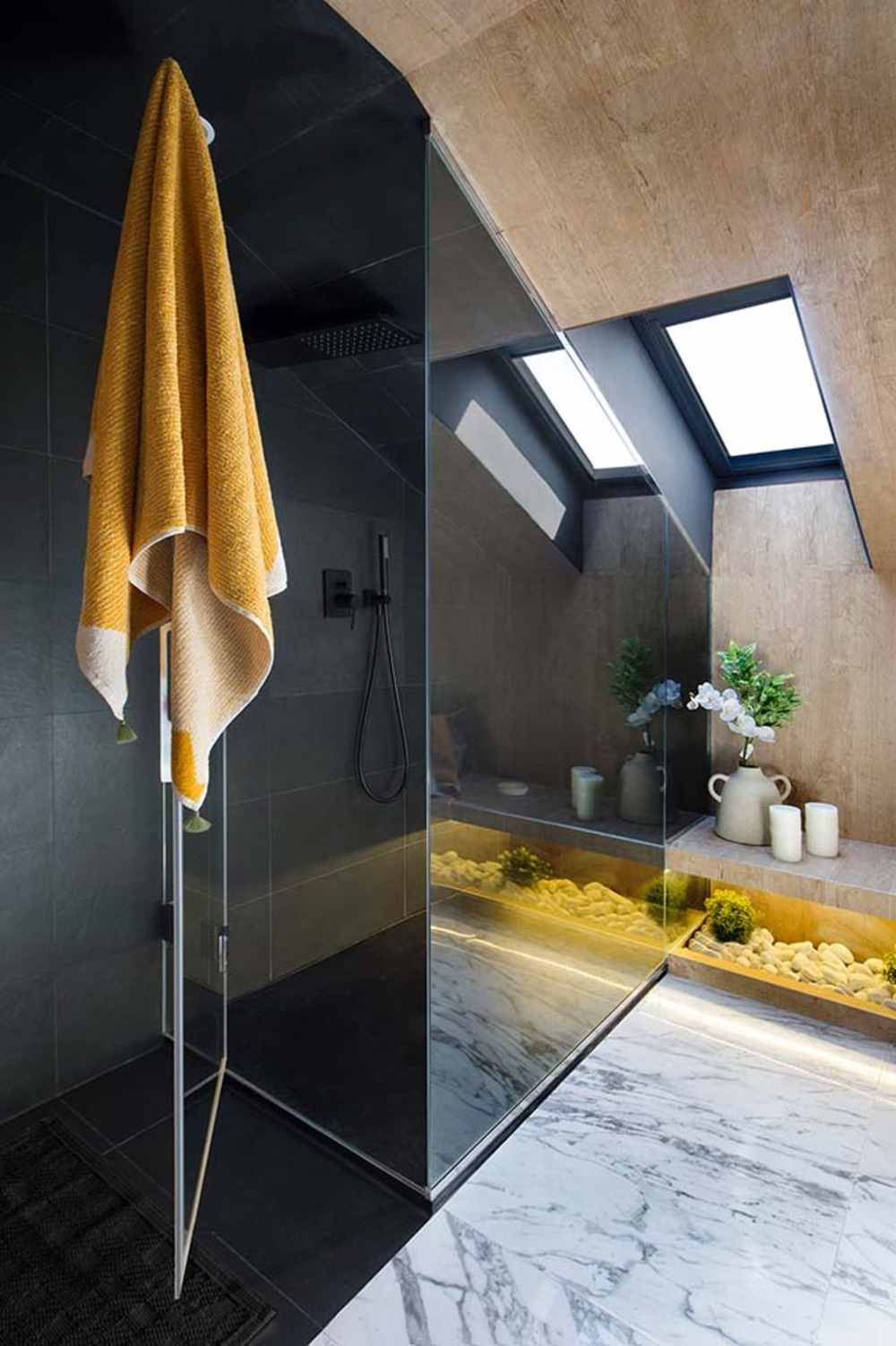 Osuška visí na sklenených dverách v sprchovacom kúte pod strešným oknom v kúpeľni s mramorovou podlahou