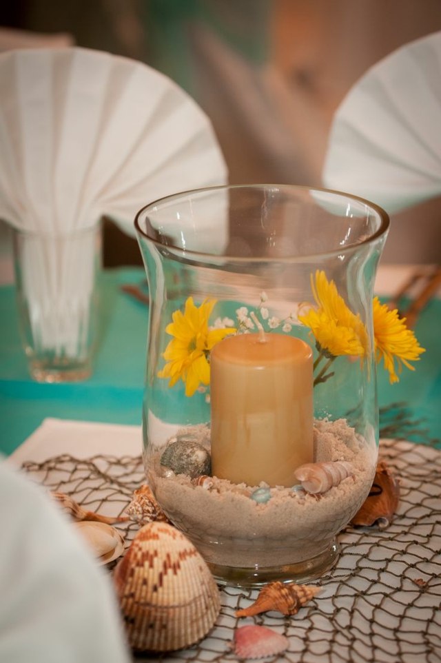 Naplňte pohár pieskom a škrupinami a vložte do neho sviečku škrupiny stola na dekoráciu sviečok z pieskového skla