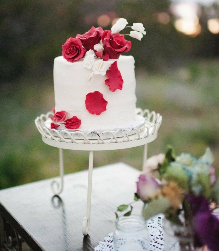 Pekný dizajn torty v bielej farbe a s červenými jedlými ružami na starožitnom stojane na tortu