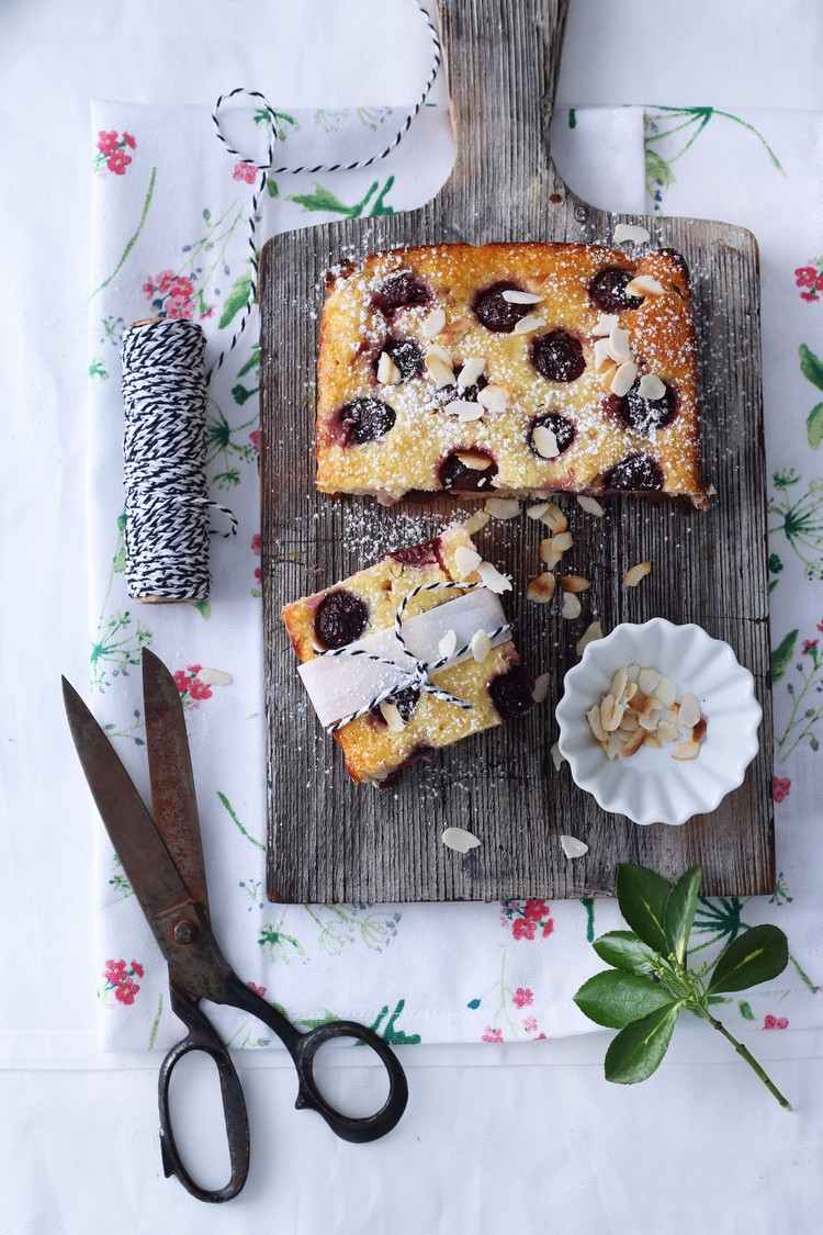 Jednoduchý čerešňový koláč z plechu, posypaný plátkami mandlí a práškovým cukrom