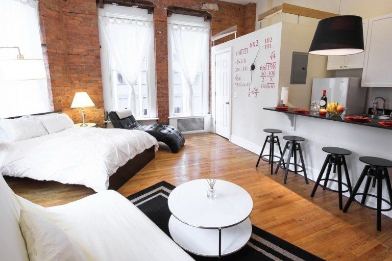 Moderný podkrovný apartmán s tehlovou stenou a bielou kuchyňou a manželskou posteľou a rohovou sedačkou
