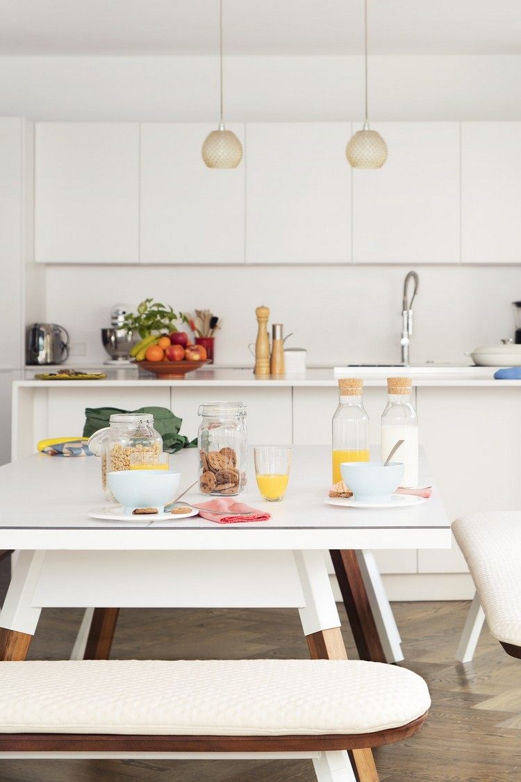 Biela jedáleň a kuchyňa so závesnými lampami a jedálenským stolom s lavicami od RS Barcelona Jedálenský stôl s lavicami, lavica, raňajky, biely interiér