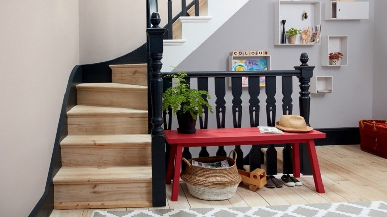 červená lavica a čierne zábradlie ako akcenty pred sivou stenou a bielymi nástennými policami