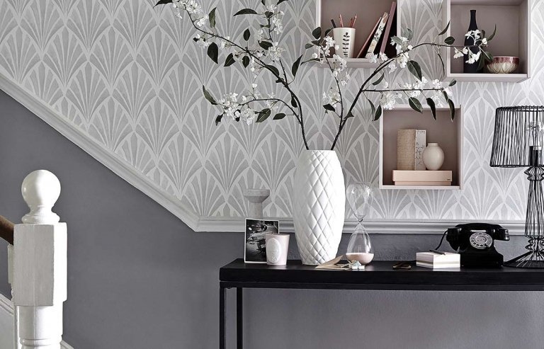 Šedá tapeta na stenu s klasickými vzormi a úzkym čiernym odkladacím stolíkom pred schodiskom