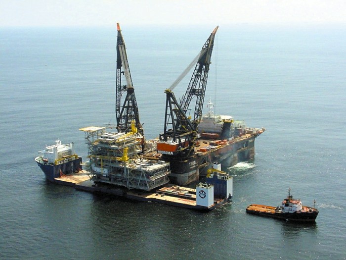 päť nadrozmerných predmetov nakladajúcich a vykladajúcich nákladnú loď na platforme, ktorá sa načítava