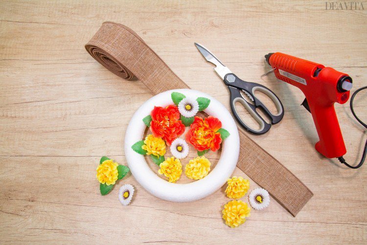 DIY veniec vyrobený z polystyrénových prsteňov, umelých kvetov a jutovej stuhy s horúcou lepiacou pištoľou