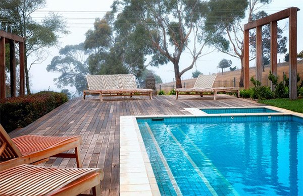 Drevená terasa zariadená ležadlami pri bazéne, vegetácia-sucho