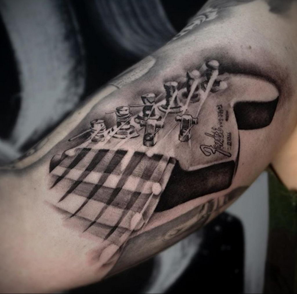 Realistyczny tatuaż na gitarze na bicepsie
