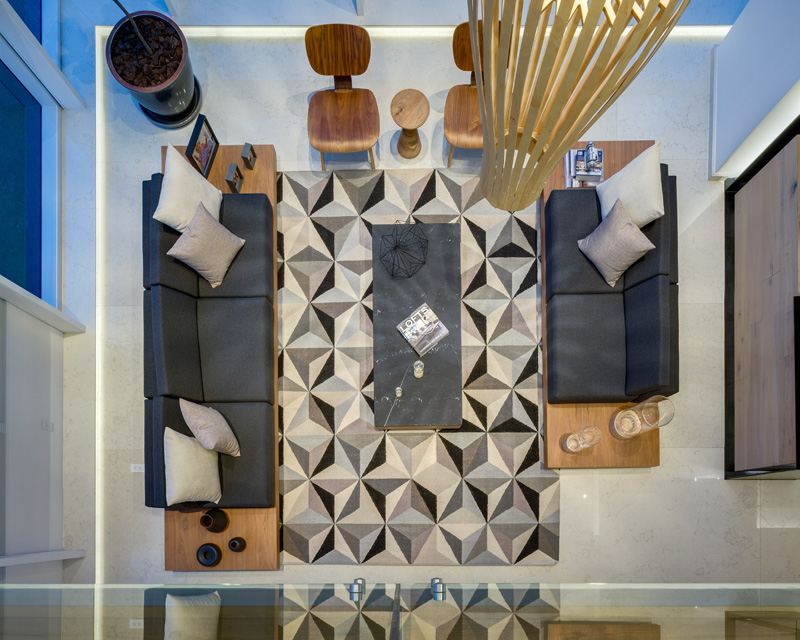 krásny výhľad z druhého poschodia penthousu velke-okno-predne-vnutorne-pohlad-nad-kobercom-geometrickymi tvarmi-sivy-pohovky-sedaci-drevo