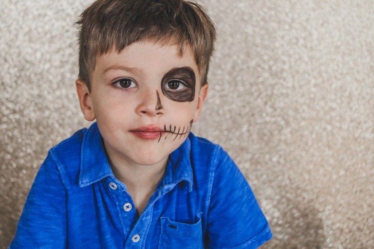 Chlapec maľujúci polovicu tváre na lebku