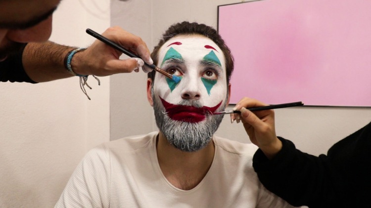 Vizážisti nanášajú na tvár bradatého muža make-up ako klaun
