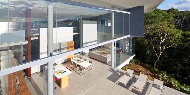 krásna terasa pokrytá prírodným kameňom vo svetlej pieskovej farbe dom-zo skla-výhľad na more-terasa-slnečná-príroda