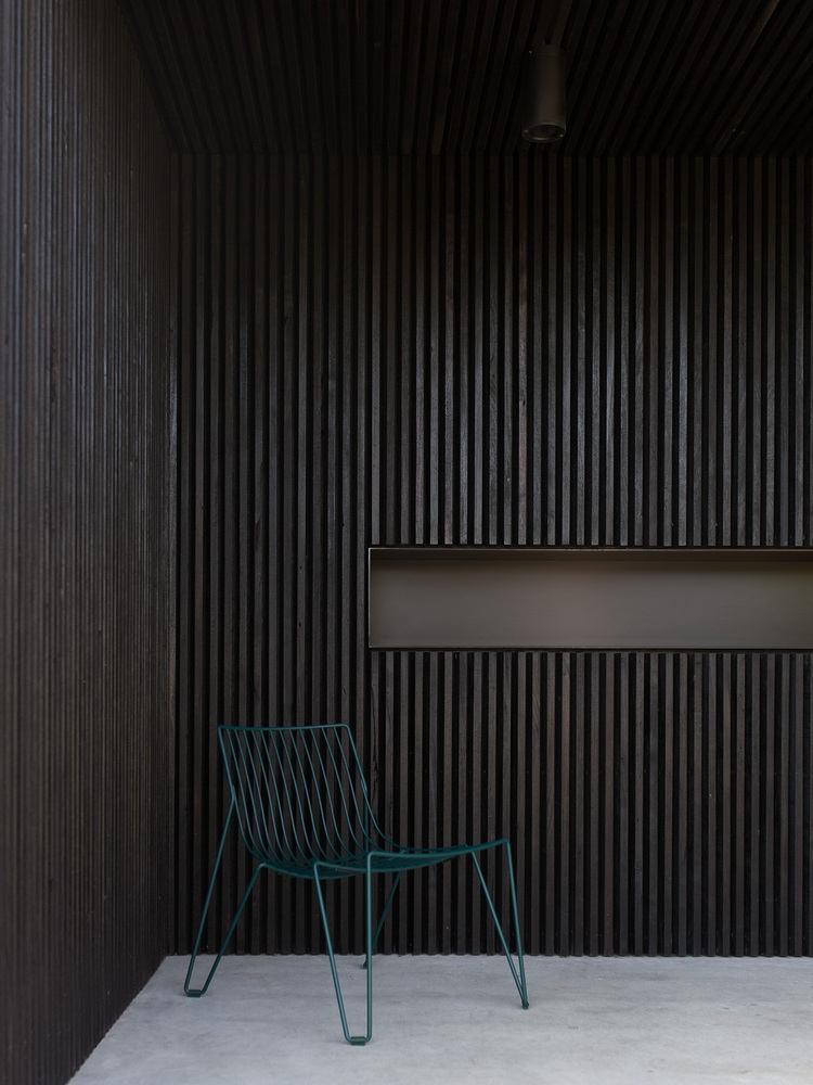 vonkajšia terasa s tmavými drevenými lamelami ako fasádny obklad s dizajnovou stoličkou v modrej farbe