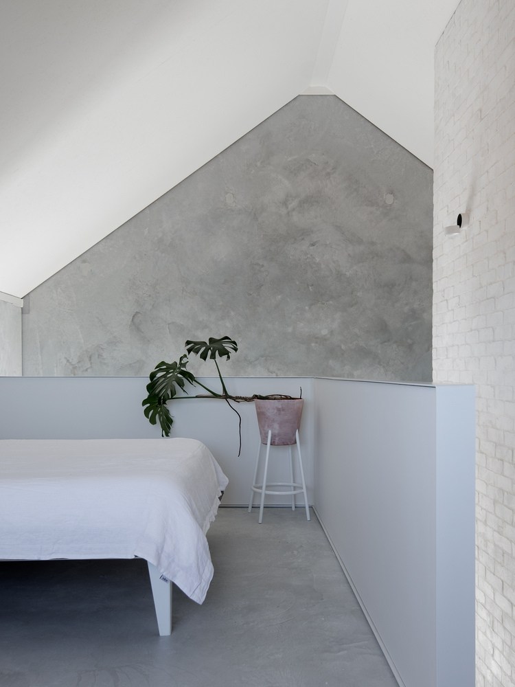 hosťovská izba s manželskou posteľou a šikmou strechou so stoličkou v rohu a gumovým stromom