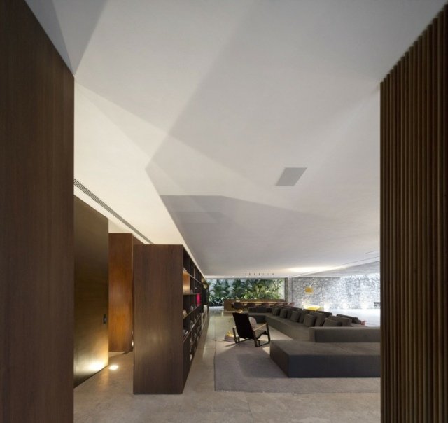 moderný interiér dom betón drevo obývacia časť priestranná Dom betónový drevo obývacia izba priestorná knižnica systém rohová sedačka