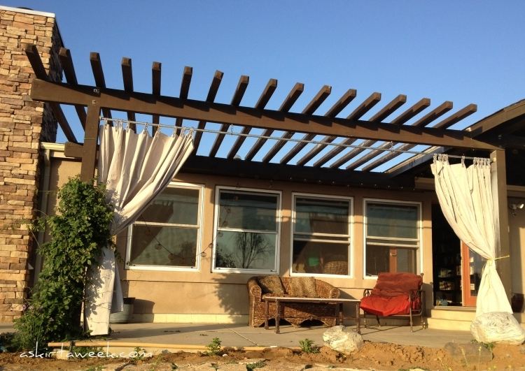 Pergola na dvore s hrubými závesmi na ochranu pred slnkom drevo-pergola-závesy-prírodný kameň-stena-drevená-konštrukcia-tmavá-gauč-kreslo-železo-ratan
