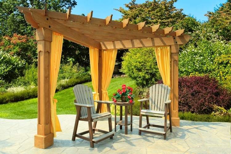 tienistý kút v záhrade s drevenou pergolou a žltými závesmi drevené-pergola-záclony-trojuholníkové-žlté-látkové-drevené-stoličky-trávnikové-kríky