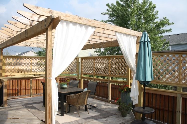 Drevená pergola s bielymi závesmi a záhradným nábytkom drevo-pergola-závesy-záhrada-ochrana súkromia-záhradný nábytok-koberec-slnečník-základ