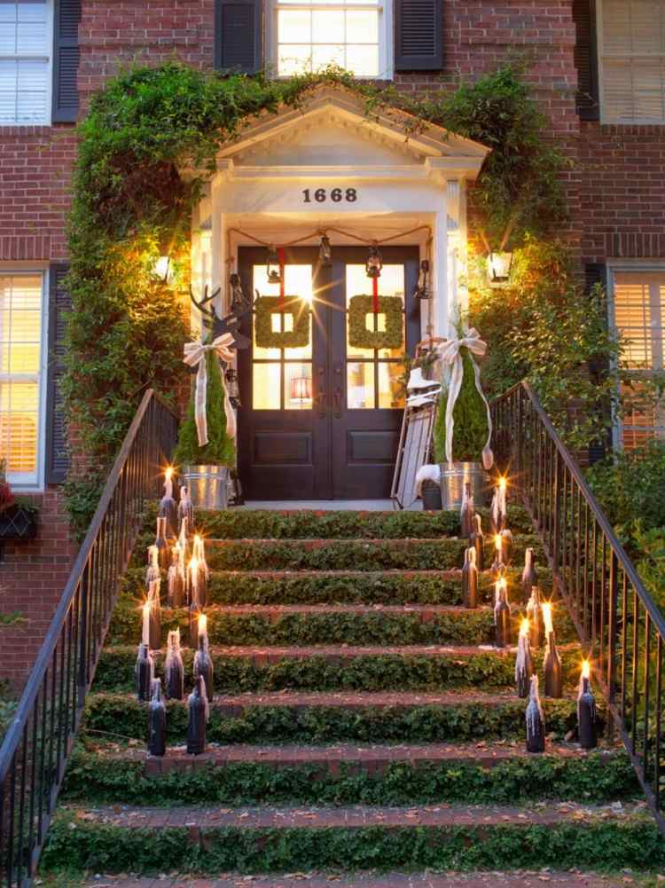 Vintage vianočné ozdoby s lampášmi a sviečkami na schodisku vianočná dekorácia zvonku-osvetlené-predné dvere-vinobranie-sviečky-fľaše na víno-schody-brečtan-kovové zábradlie