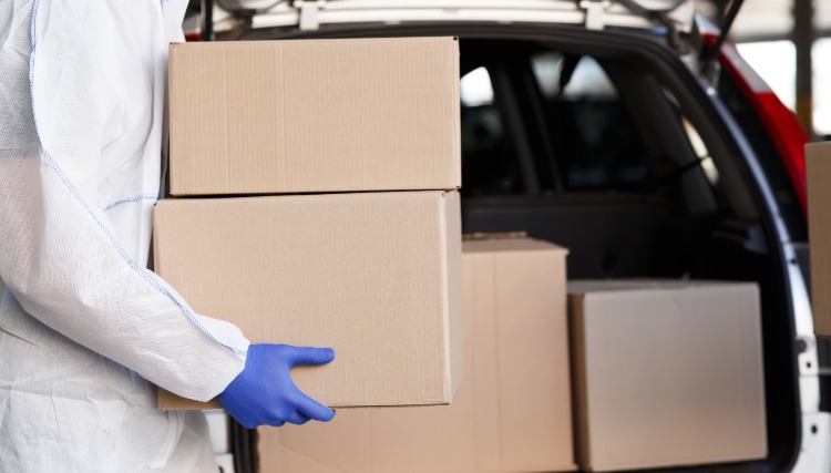 muž v ochrannom odeve nosí v aute kartónovú škatuľu