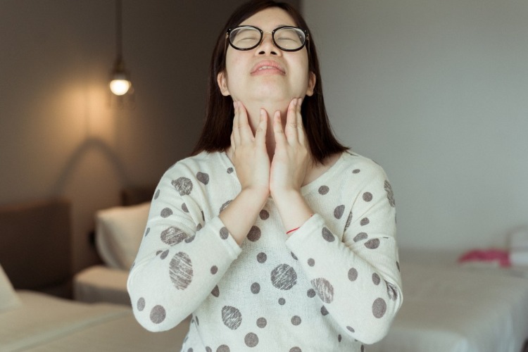 Ázijská žena držiaca sa za krk kvôli problémom so štítnou žľazou pri hypotereóze