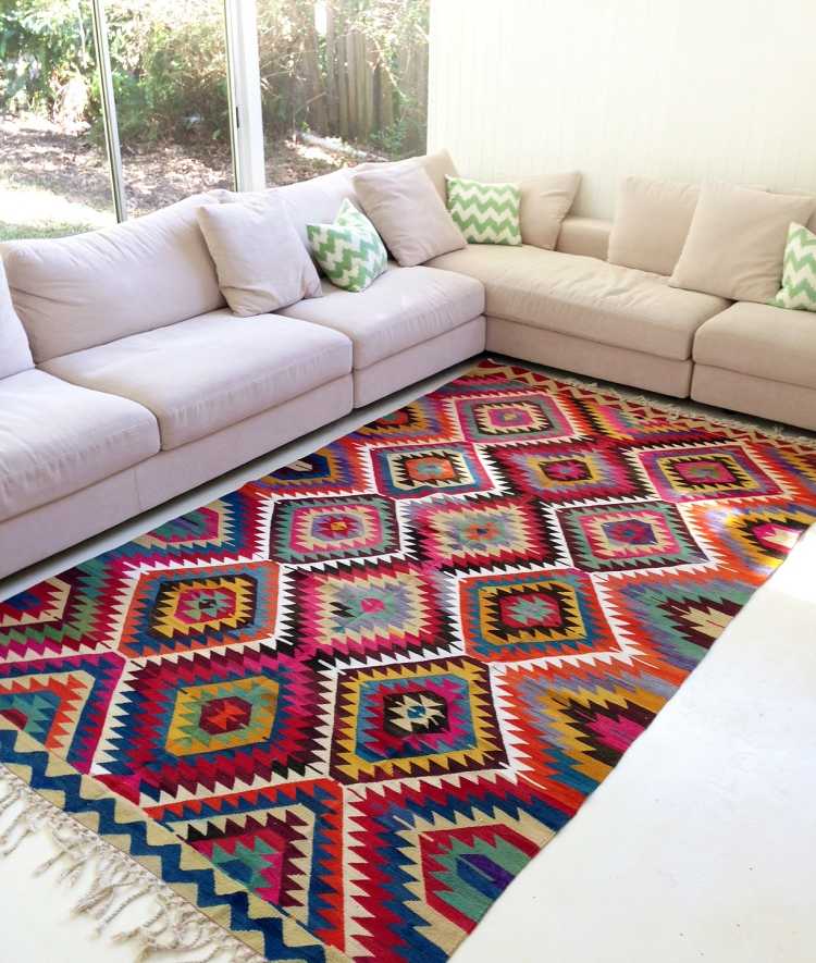 neutrálny čalúnený nábytok a pestrý kilimový koberec Kilim-koberec-moderná-rohová-pohovka-vzor-farebné-sivé-vankúše-čalúnenie-okenná stena