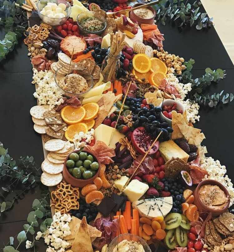 Veľký syrový tanier s množstvom ovocia, zeleniny a občerstvenia Podávajte syrový tanier veľké-pukance-olivové-misky-kiwi-zelenina-omáčka-humus-soľné tyčinky-tortilla-chipsy-plátky pomaranča-2