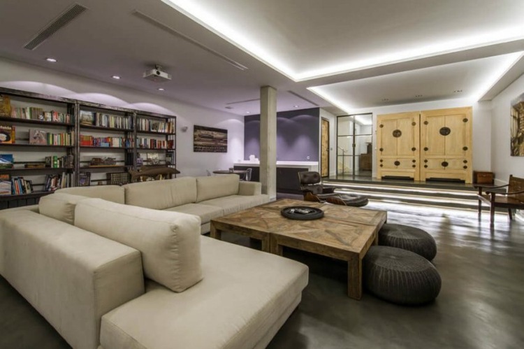 Podkrovný nábytok-nástenná polica-drevené-knihy-stropné žiarovky-betónové podpery-pohovka-béžová-látka-poťah-konferenčný stolík-ratanová stolička-čierna-6