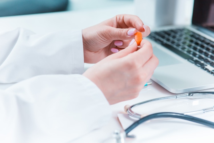 lekár drží pred svojim notebookom oranžovú pilulku