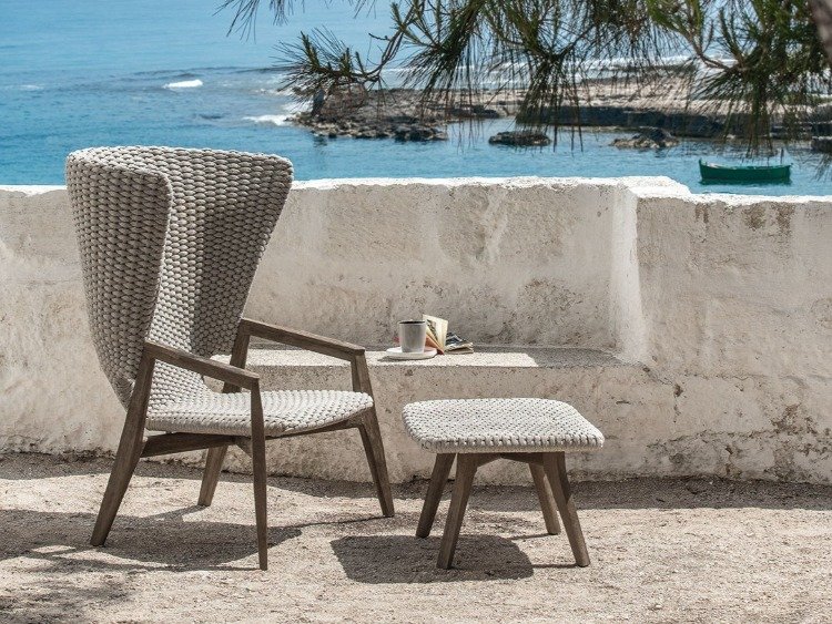 veľká teaková stolička s okolitým operadlom a taburetkou v záhrade