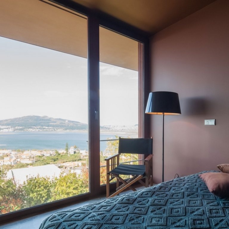 dizajn miestnosti-hnedá-spálňa-stena-farba-strop-tyrkysová-stolička-podlahová lampa-okno-stena-výhľad-mesto-more