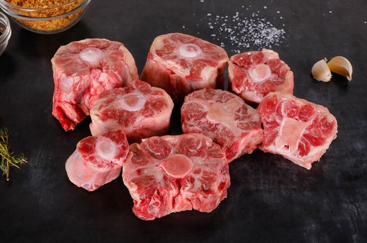 Surový chvost na kosti na stole s strúčikmi cesnaku a korením pripravený na varenie