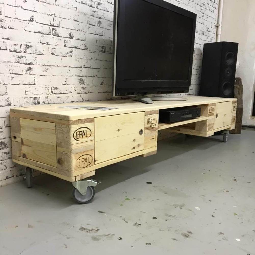 Rustikálna paletová televízna skrinka s DVD prehrávačom s plochou obrazovkou a reproduktormi pred bielou tehlovou stenou