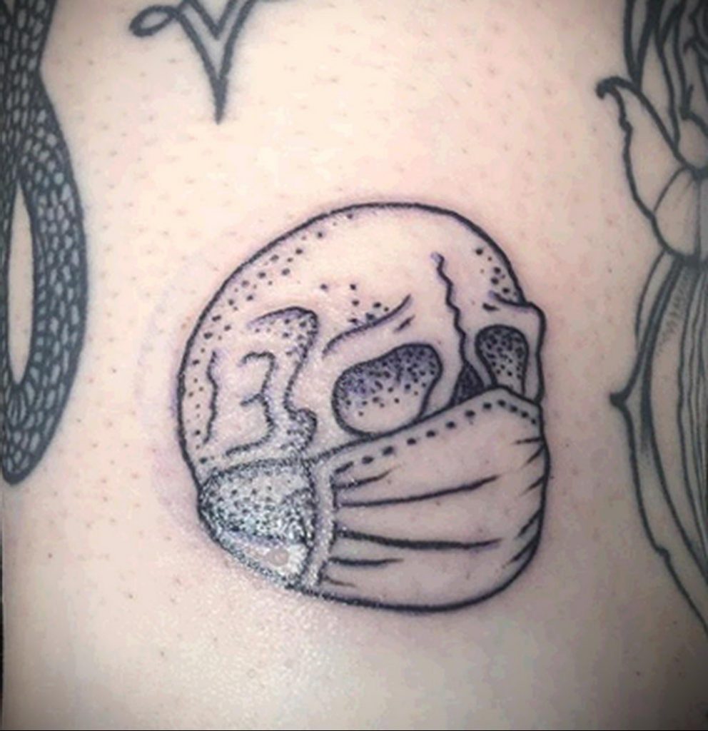 Tetovaža na temu koronavirusa COVID -19 - lubanja u sterilnoj maski