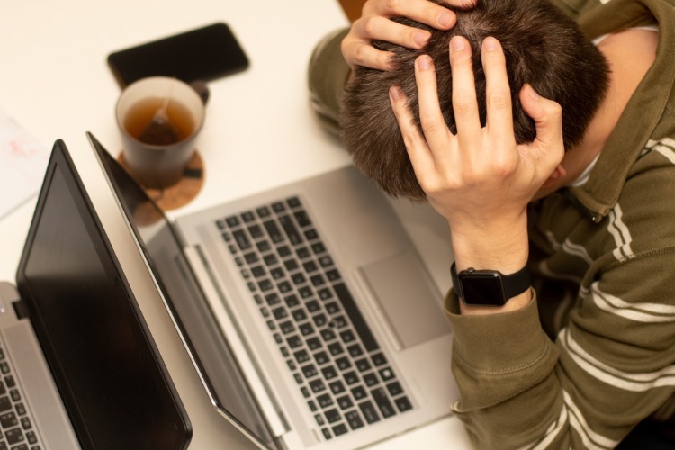 frustrovaný mladý muž sediaci pred prenosným počítačom a držiaci sa za hlavu