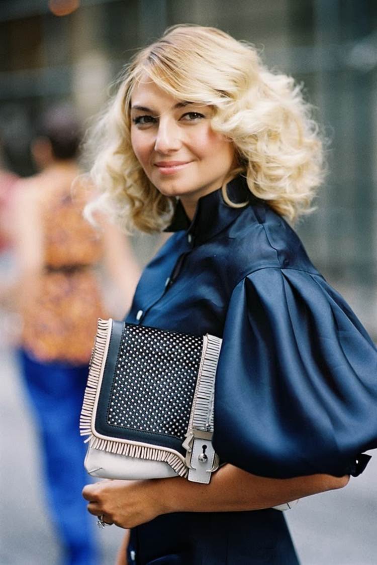 Rukávy zo saténovej blúzky kombinujú tmavomodrú trendovú bielu koženú tašku s blond vlasmi