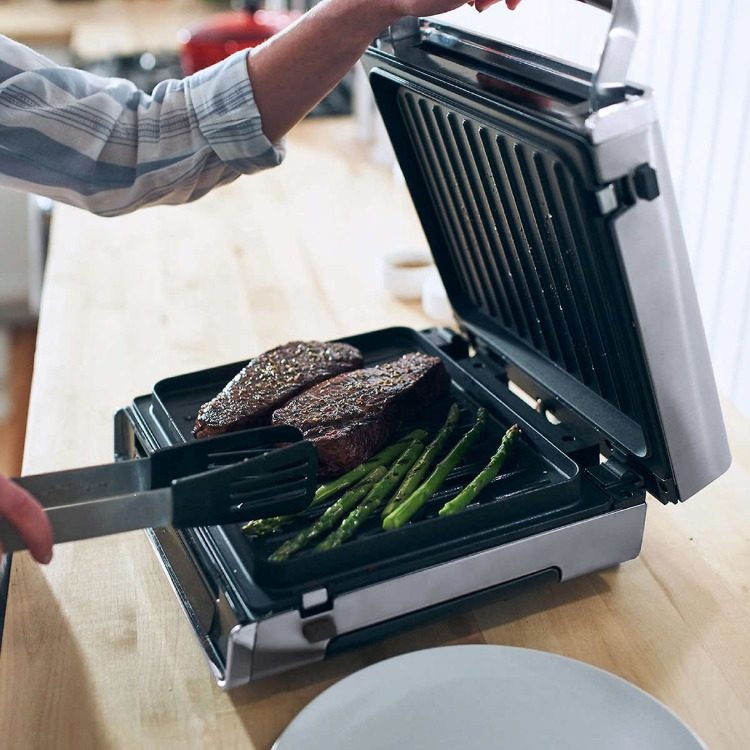 človek griľuje zelenú špargľu a steaky na kontaktnom grile v pohodlnom vnútornom grile