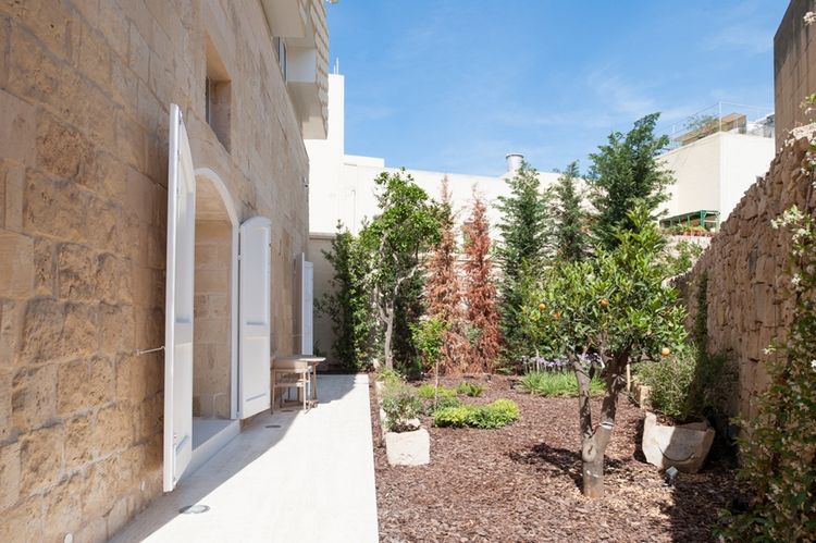 kamenná fasáda s otváracími dverami a dvorom so záhradnými rastlinami a ovocím