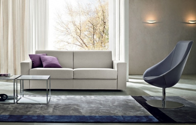 Dve gauče vo svetlo šedej farbe a vankúše vo fialovej farbe Rozkladacia pohovka zo sivých závesov-obyčajného kresla-koberca-bočných stolíkov-osvetlenia-okennej steny