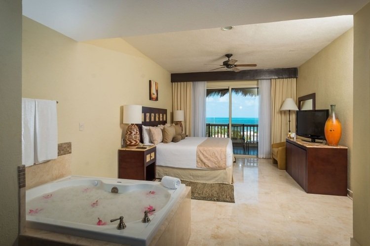 Posteľ umiestnená na základni a vírivke v miestnosti spálňa-vírivá vaňa-hotelová izba-kachľová základňa-posteľ-terasa-výhľad-more-televízia