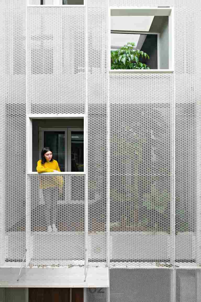 žena pozerá von z otvoru na terase s perforovanou fasádou domu