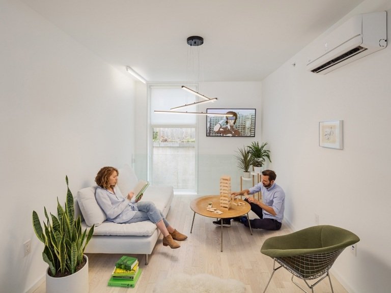 pár sediaci v úzkej obývačke s klimatizáciou a gaučom