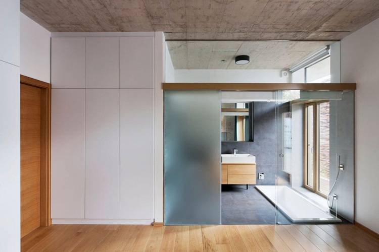 Sklenená priečka oddeľuje spálňu od kúpeľne kúpeľňa-moderná-sklenená-stena-matné sklo-betón-strop-drevo